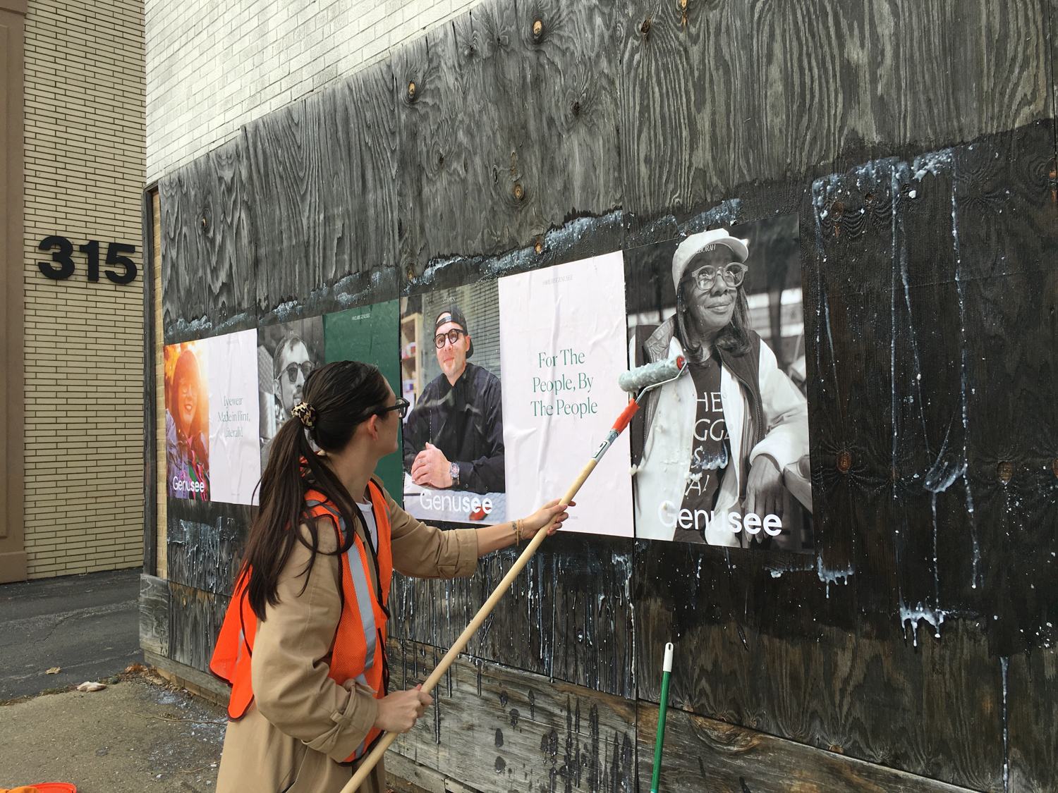Wheatpasting a Genusee poster onto a boarded-up building